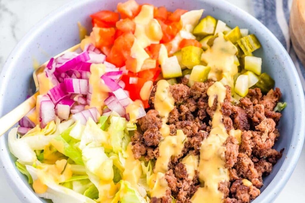 ground beef, lettuce, tomatoes, pickles, and sauce in a bowl.