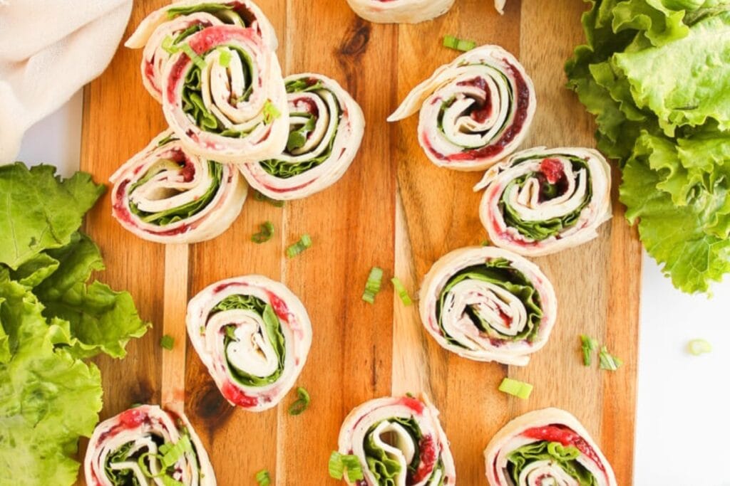 Cold turkey pinwheels with cranberry sauce on a wooden board.