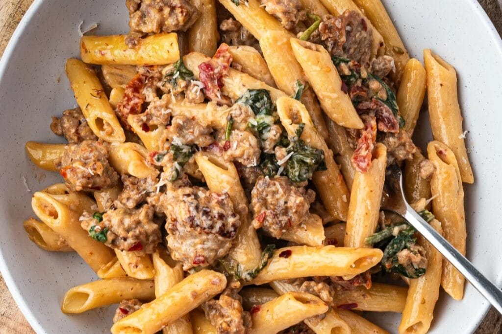 Creamy sausage pasta with kale and burrata in a bowl.