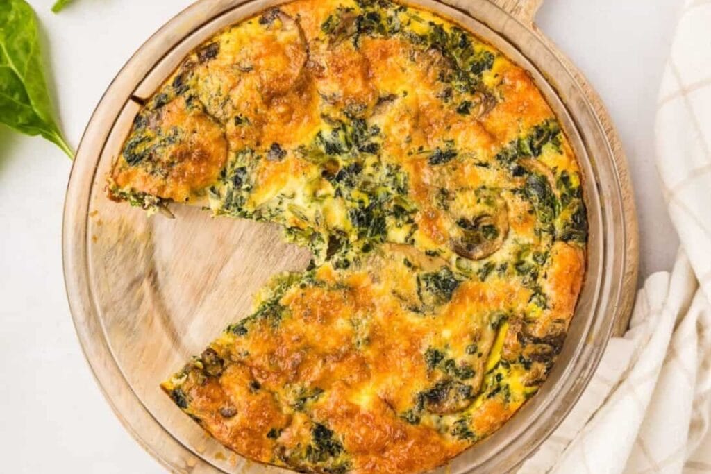 Crustless spinach quiche on a round wooden pizza board.