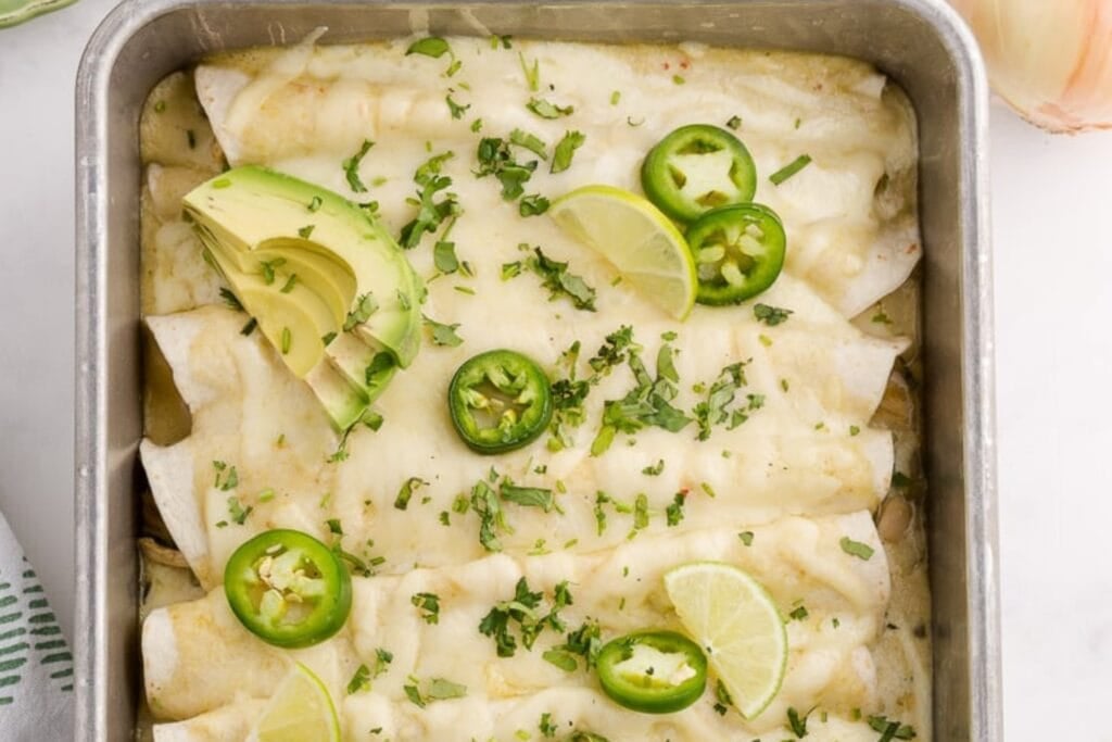Green chicken enchiladas with flour tortillas in a baking dish.