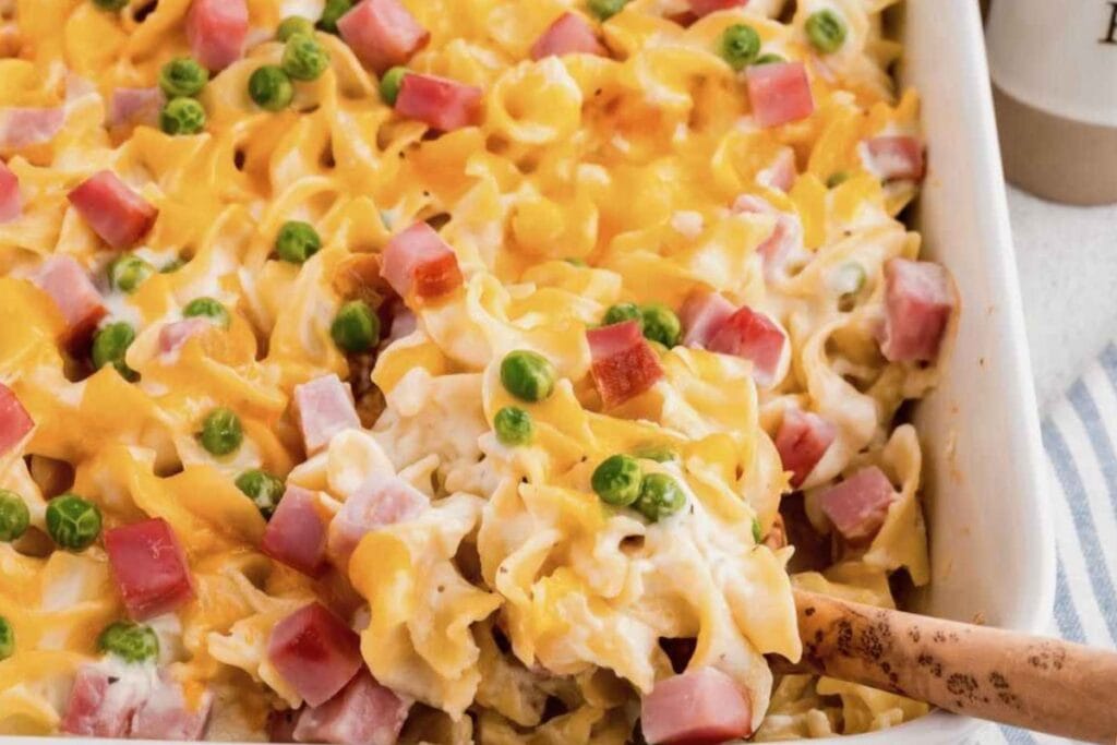 Ham and noodle casserole in a baking dish with a wooden spoon.