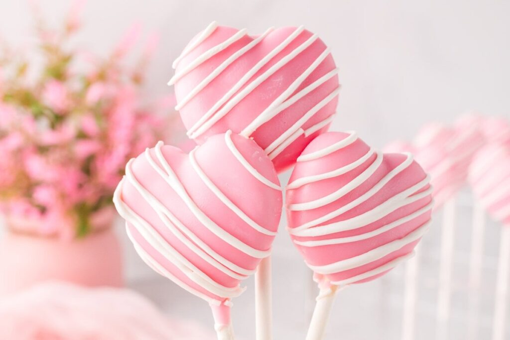 Pink heart cake pops drizzled with white chocolate.