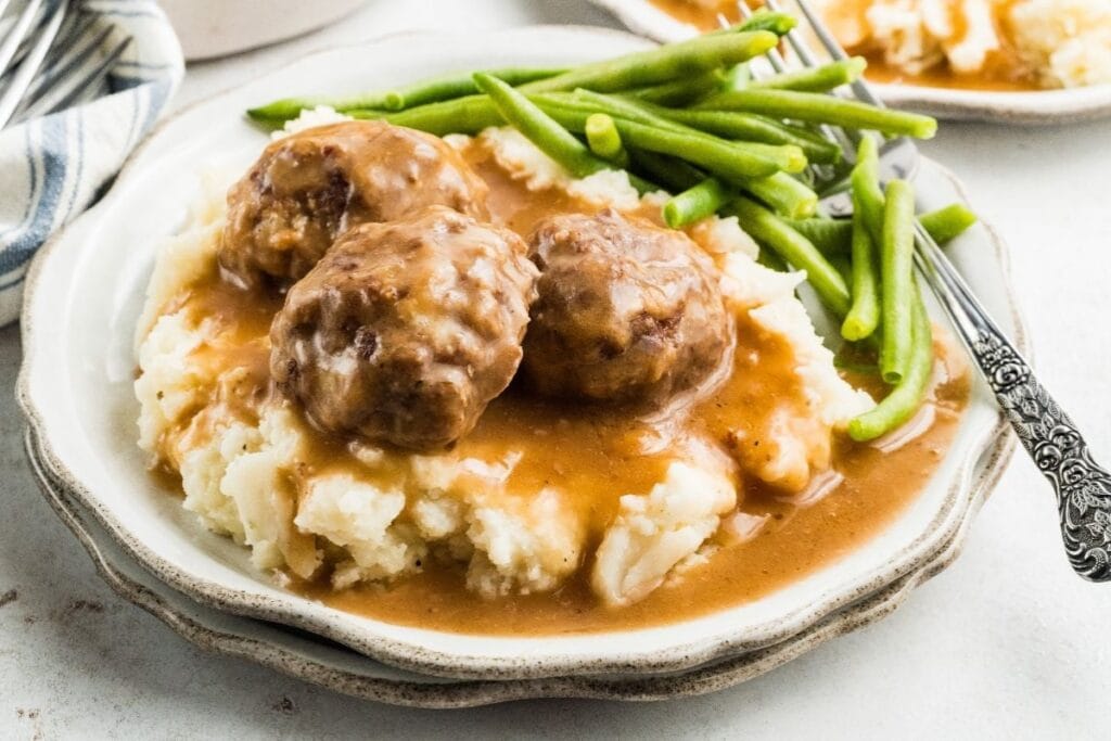 Meatballs in gravy served with green beans on a plate.
