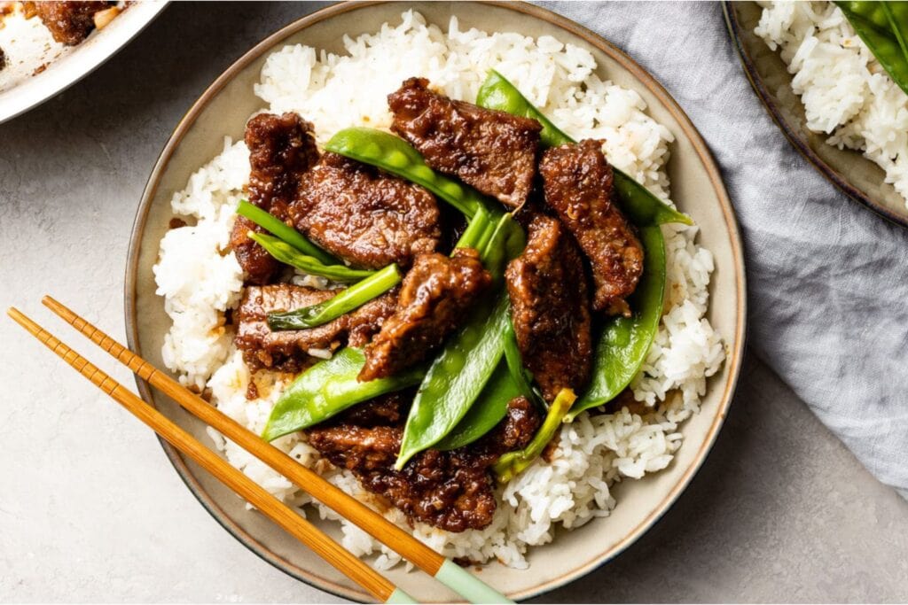 Mongolian beef with snow peas over rice on a plate.