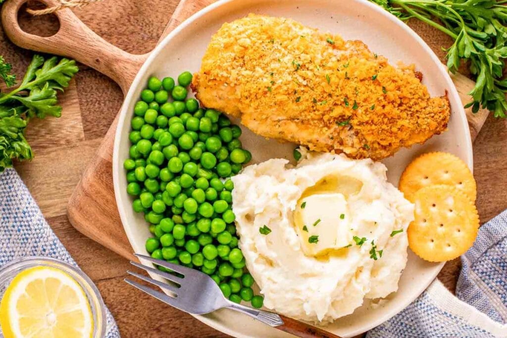 Ritz cracker chicken with mashed potatoes and peas on a plate.