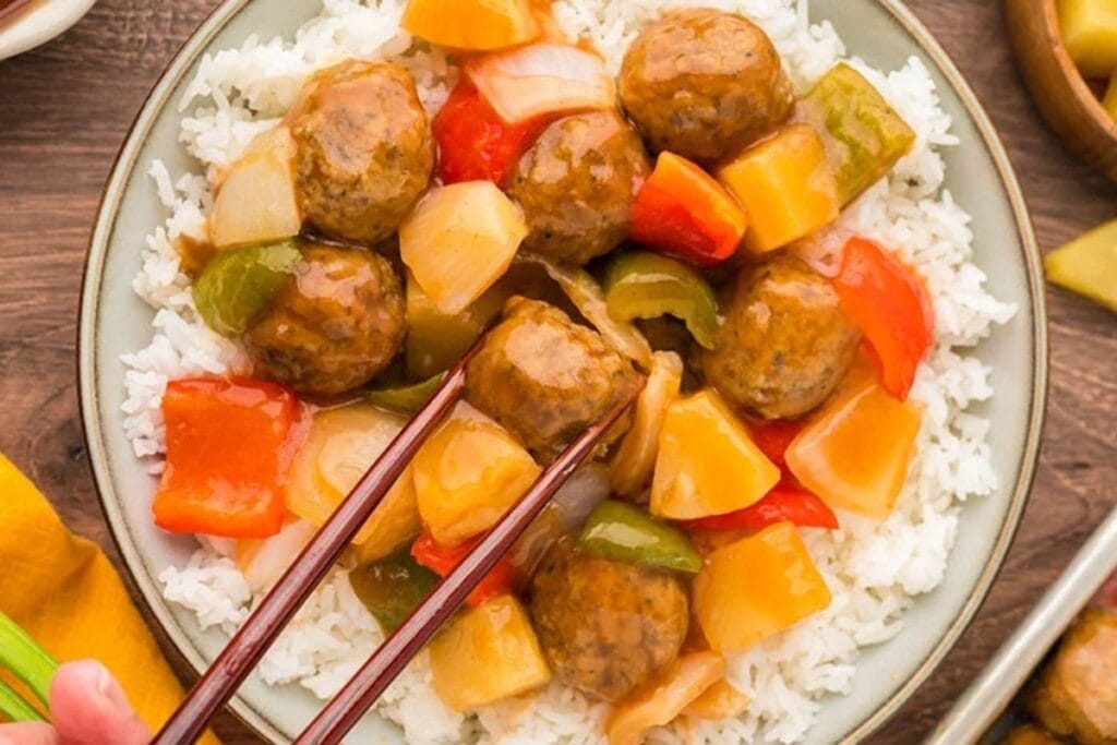 Sweet and sour meatballs in a bowl over rice.