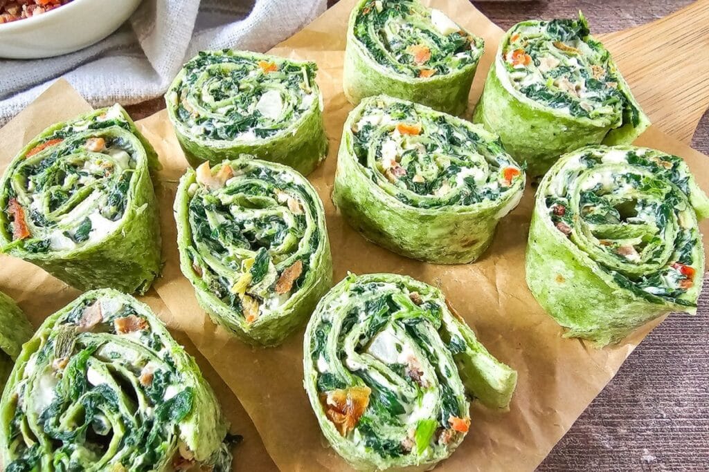 Spinach dip pinwheels on a wooden board with parchment paper.