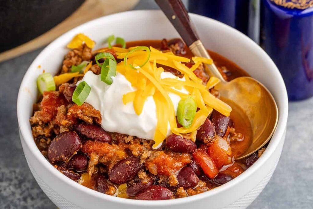 Stove top chili topped with cheese and sour cream in a bowl.