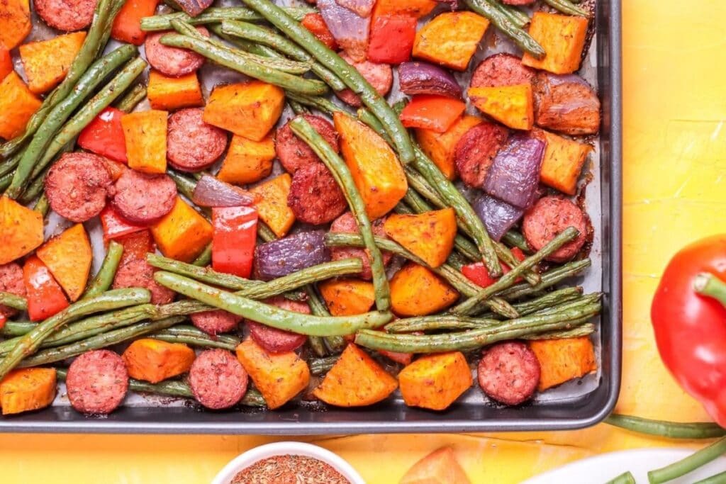 A close up shot of sheet pan sausage and sweet potatoes.