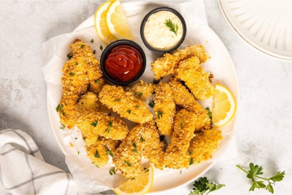 Homemade fish sticks with dipping sauces on a plate.