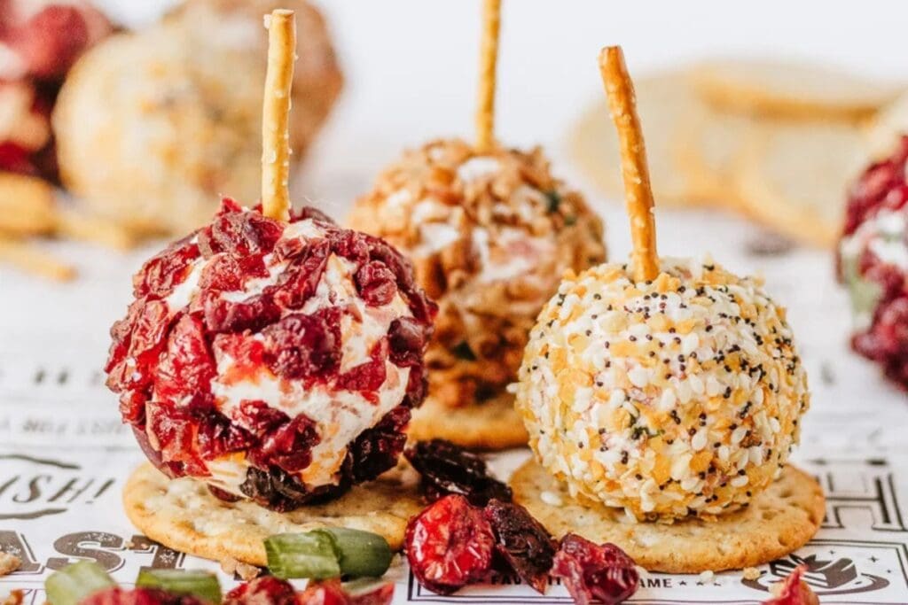 Mini cheeseball bites with pretzel sticks served on crackers.