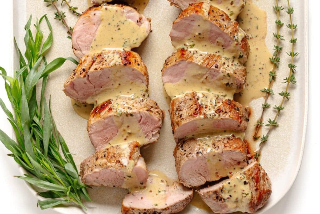 Pork tenderloin with mustard sauce on a plate.
