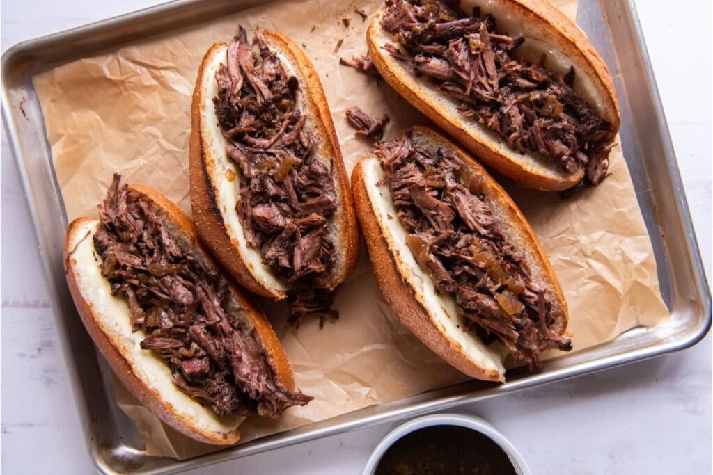 Slow cooker French dip sandwiches arranged on a sheet pan.