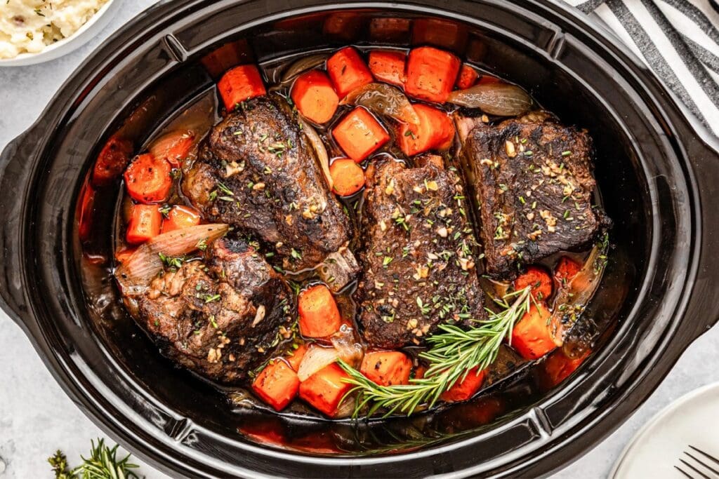 Slow cooker short ribs with carrots and herbs in a savory sauce.