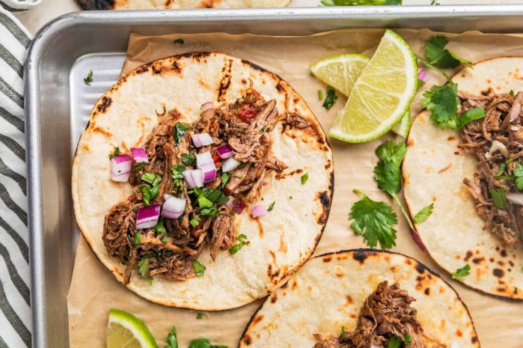 Slow cooker shredded beef tacos arranged on a sheet pan.