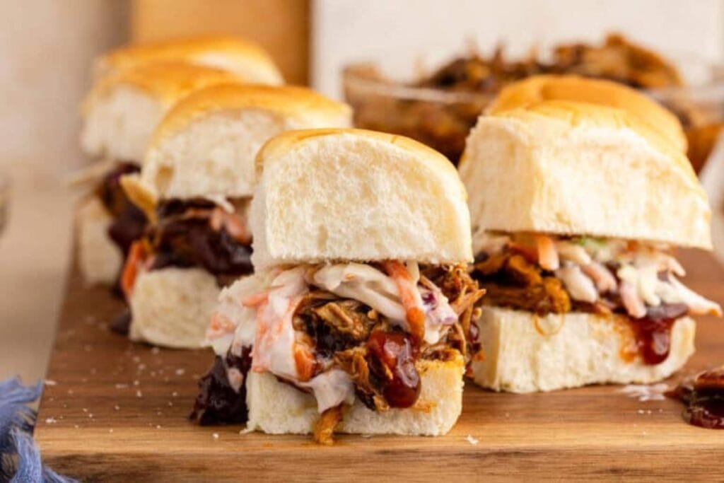 Pulled pork sliders on Hawaiian rolls on a wooden board.