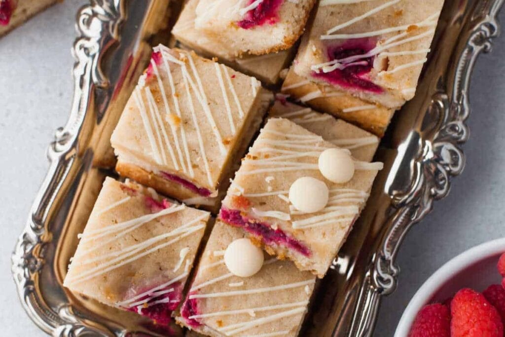 White chocolate raspberry blondies cut into squares on a decorative tray.