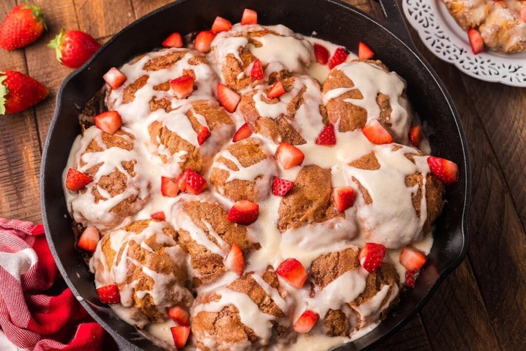 Baked French toast with maple glaze and strawberries in a skillet.