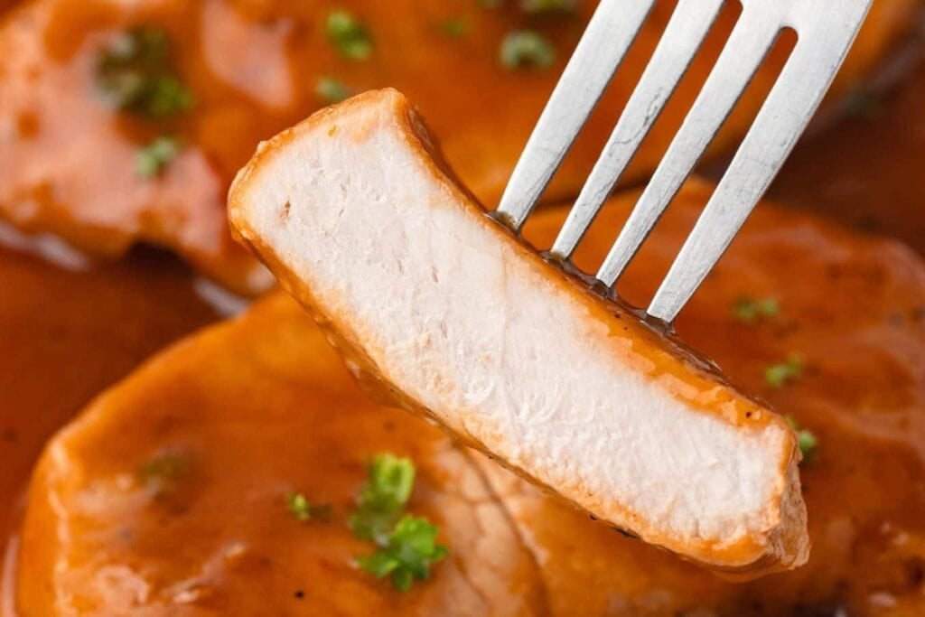 Close-up of a saucy pork chop on a fork.