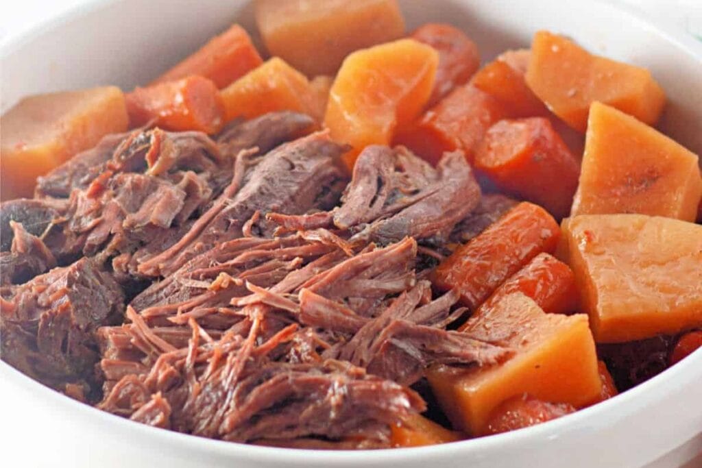 Beef chuck roast with carrots and potatoes in a bowl.