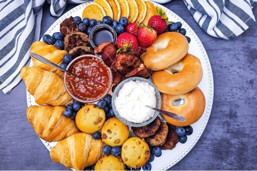 Breakfast charcuterie board with croissants, bagels, fruit, and dips.