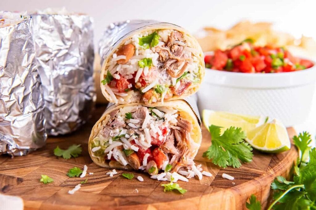 Carnitas burrito cut in half on a wooden board.