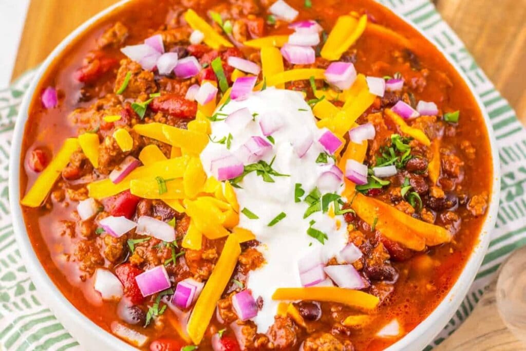 Dr Pepper chili in a bowl topped with cheese and onions.