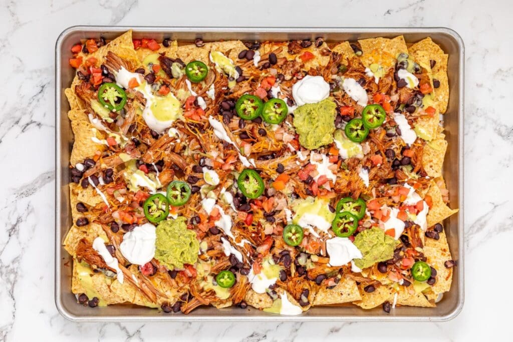 Loaded pulled pork nachos on a baking sheet.