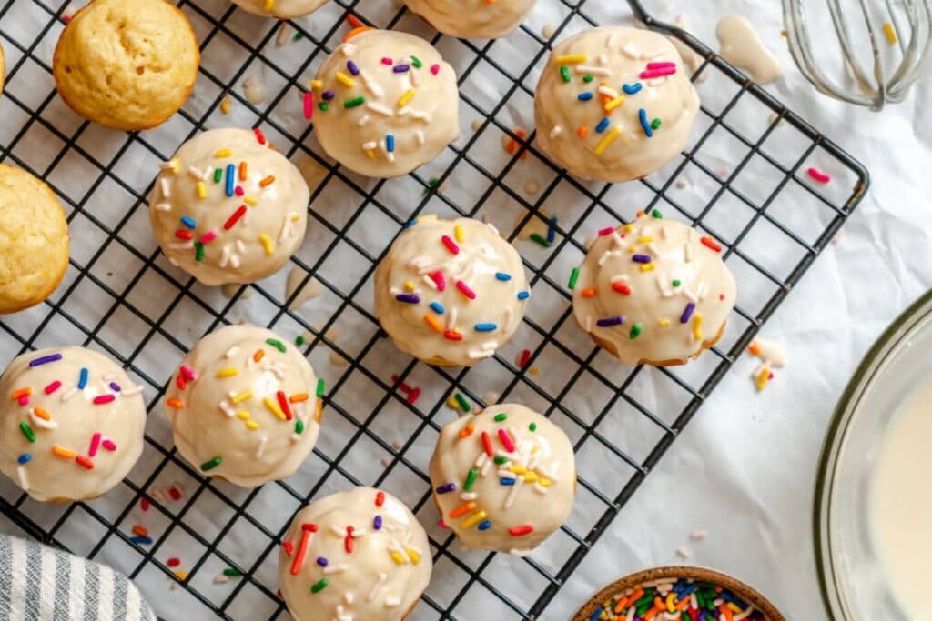 Sugar cookie donut muffins with glaze and sprinkles on a cooling rack.