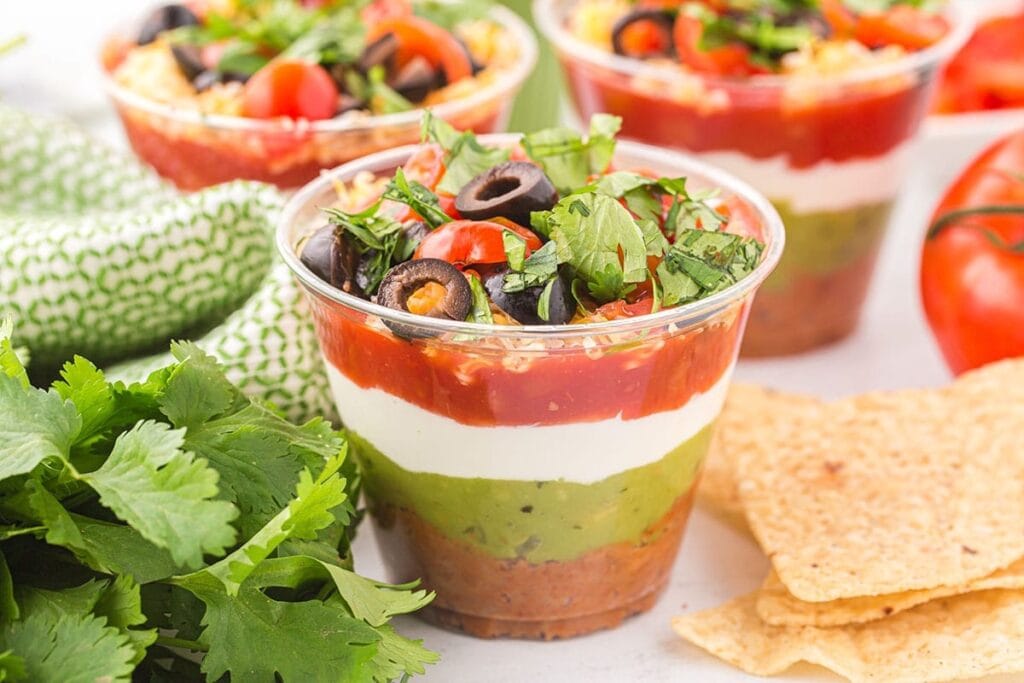 7-layer dip cups topped with olives, tomatoes, and cilantro.