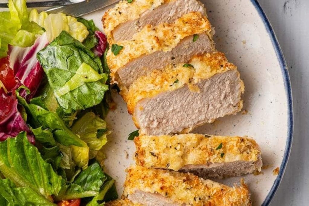 Air fried pork chops sliced on a plate with side salad.