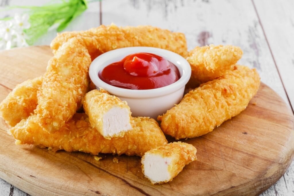 Breaded chicken tenders with dipping sauce on a board.