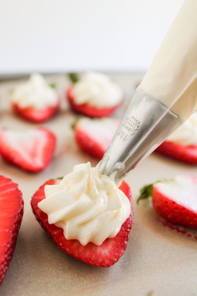 Piping cheesecake filling onto strawberries.