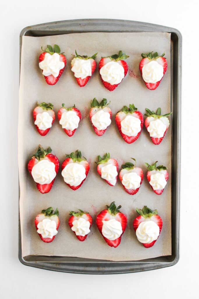 Strawberry halves with cheesecake filling on a sheet pan.