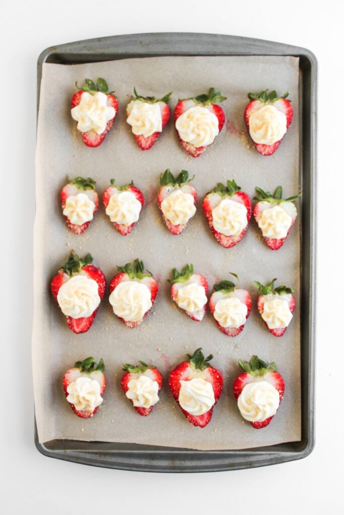 Cheesecake deviled strawberries with crumbs on a sheet pan.