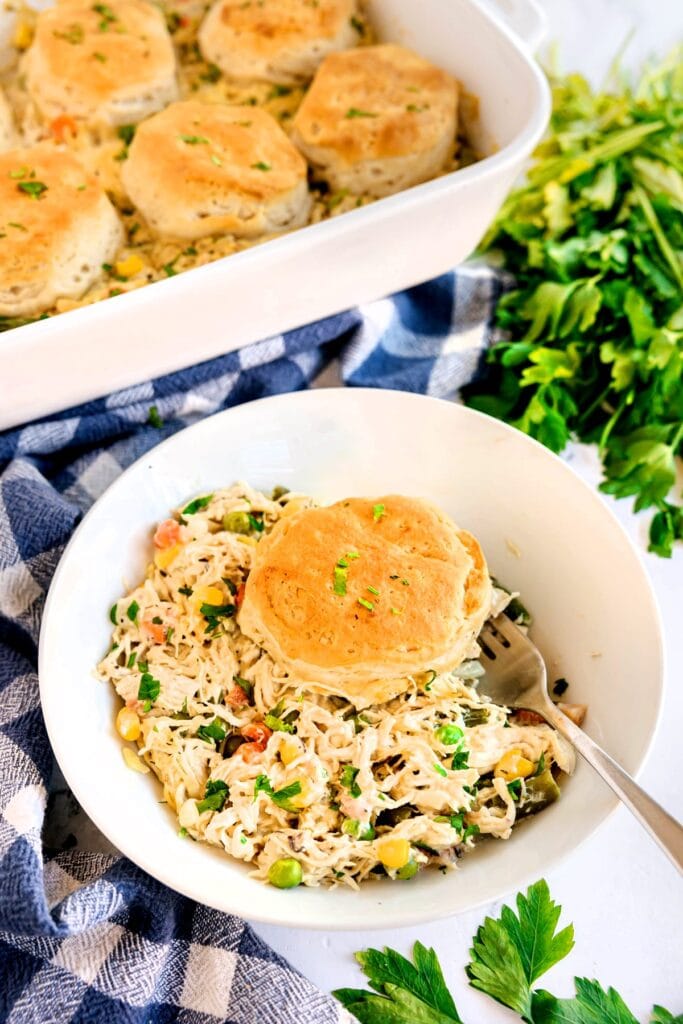 Chicken pot pie casserole topped with a flaky biscuit in a bowl.