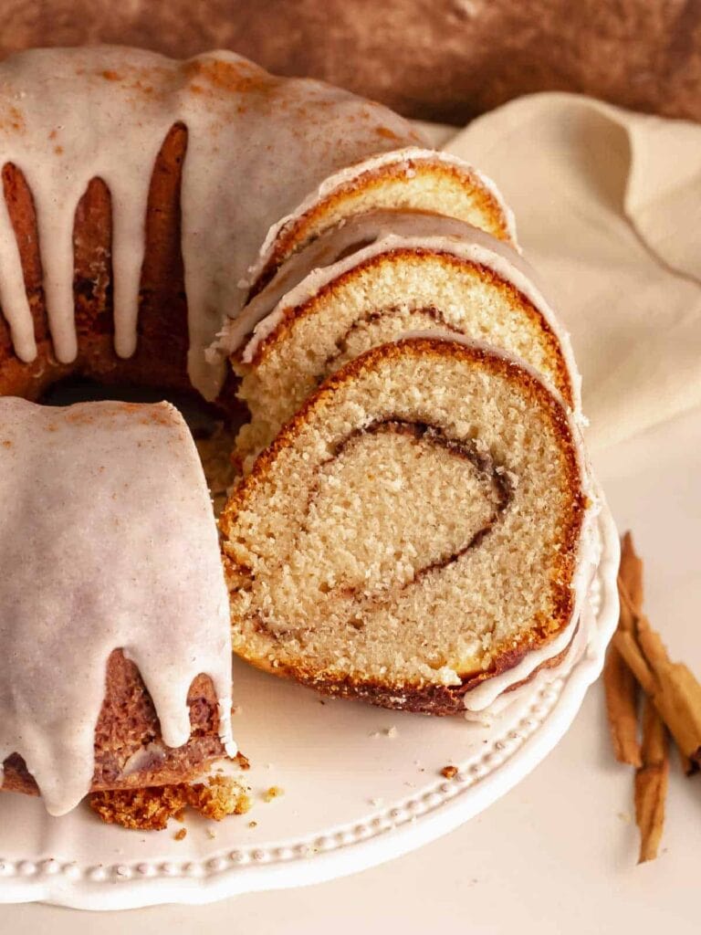 Sliced cinnamon Bundt cake with cinnamon swirl and vanilla glaze on a cake stand.