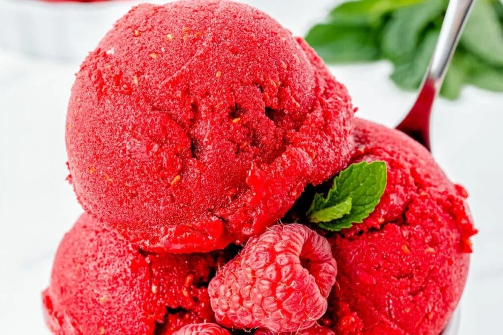 Raspberry sorbet scoops with fresh raspberries.