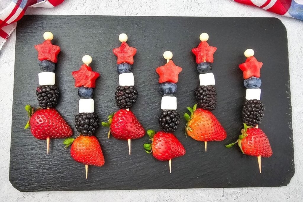 Red white and blue fruit kabobs on a serving board.