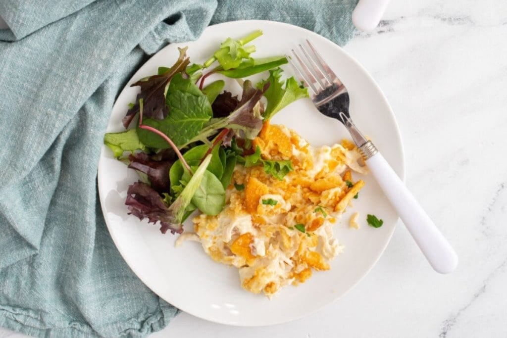 Million dollar chicken casserole served on a plate with a side salad.