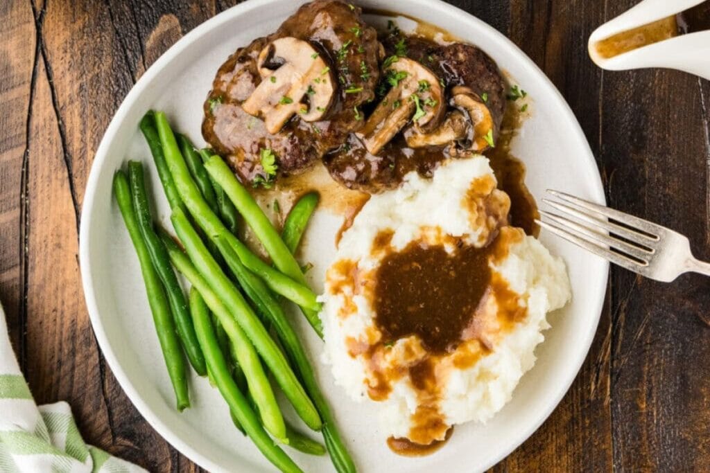Salisbury steak with mashed potatoes and green beans on a plate.