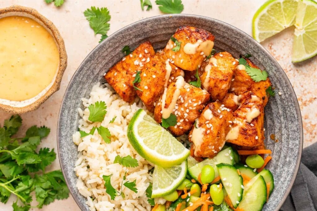 Salmon bites served over rice with vegetables in a bowl.