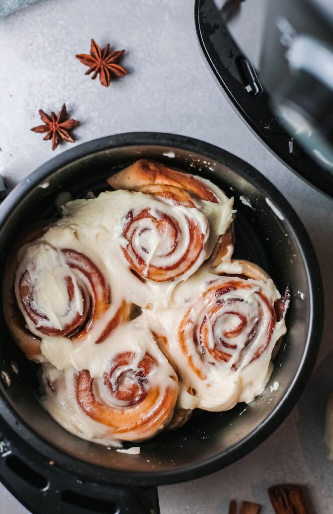 Air Fryer Cinnamon Rolls with butter frosting in an air fryer basket.