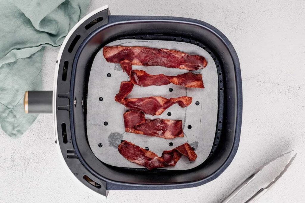 Crispy turkey bacon in an air fryer basket.