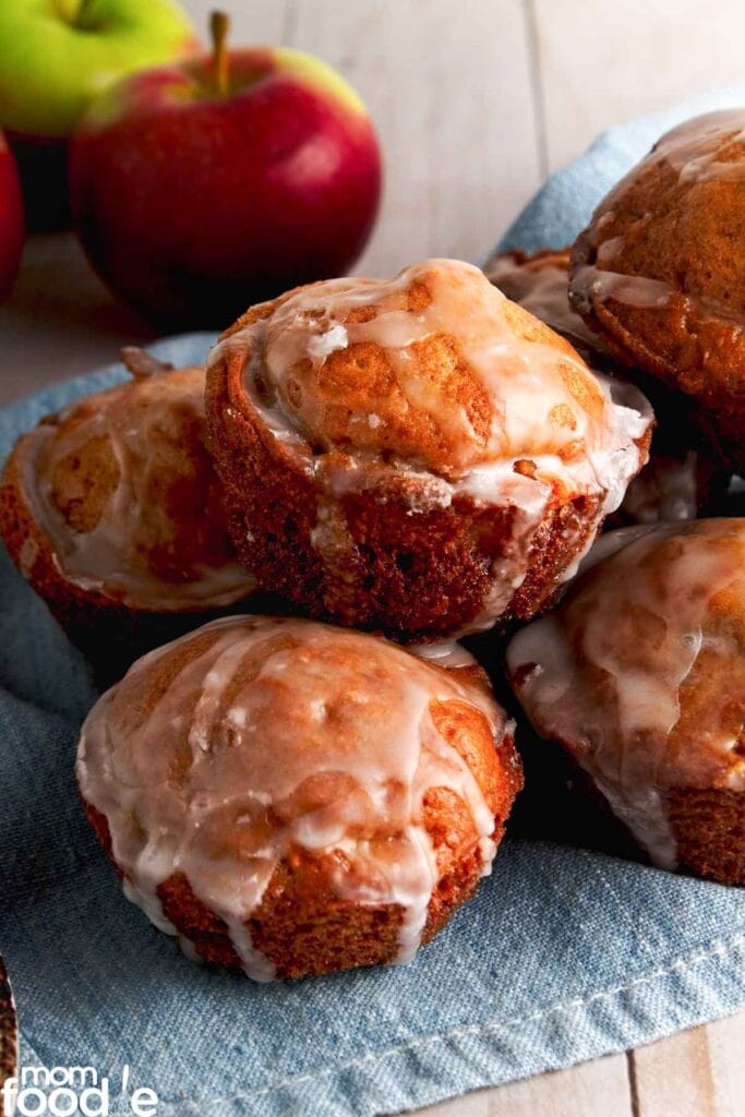 Baked apple fritters with glaze on a cloth-lined surface.