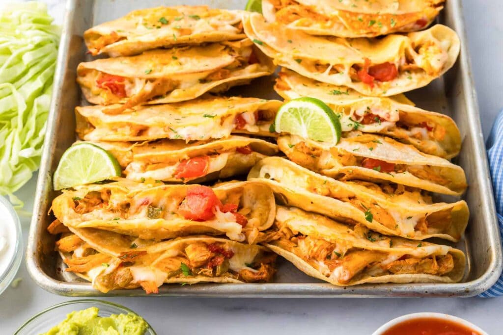 Crispy baked chicken tacos stacked on a baking sheet.