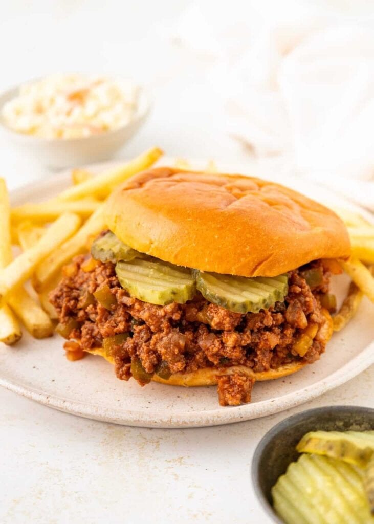 Sloppy Joe sandwich with pickles and fries on a plate.