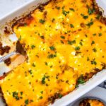 John Wayne Casserole casserole topped with melted cheddar cheese and parsley in a baking dish.