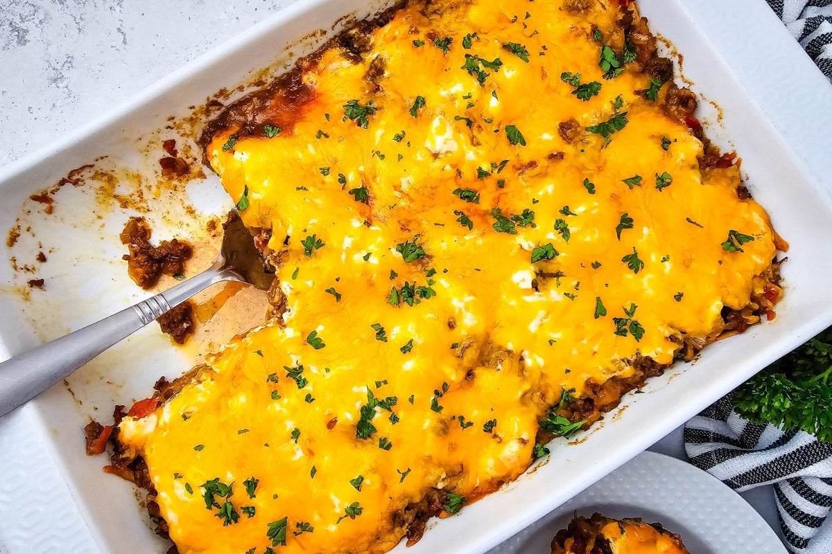 John Wayne Casserole casserole topped with melted cheddar cheese and parsley in a baking dish.